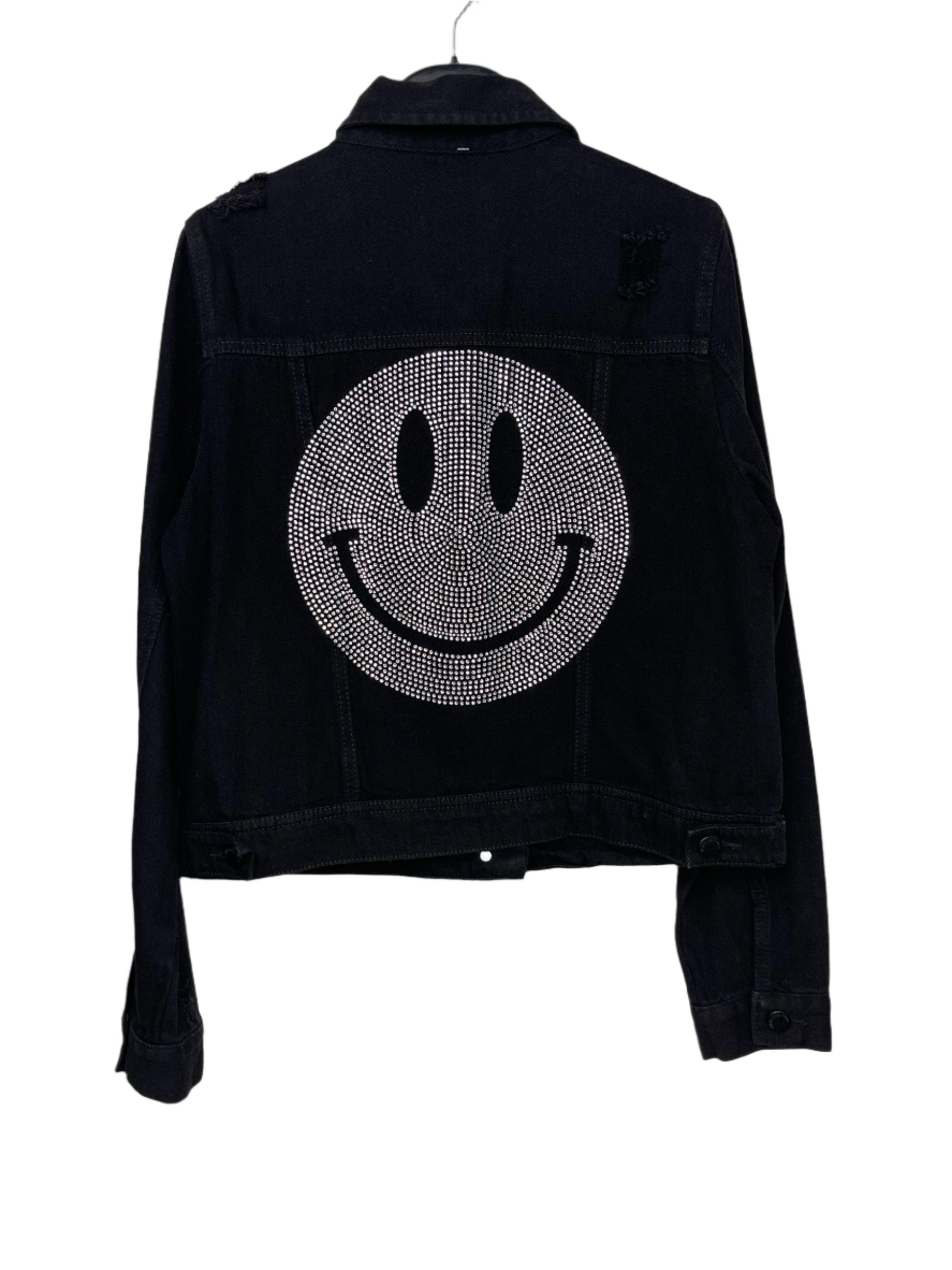 A black denim jacket with a crystal silver smiley design on the back, featuring a pointed collar, button front, and front flap pockets.